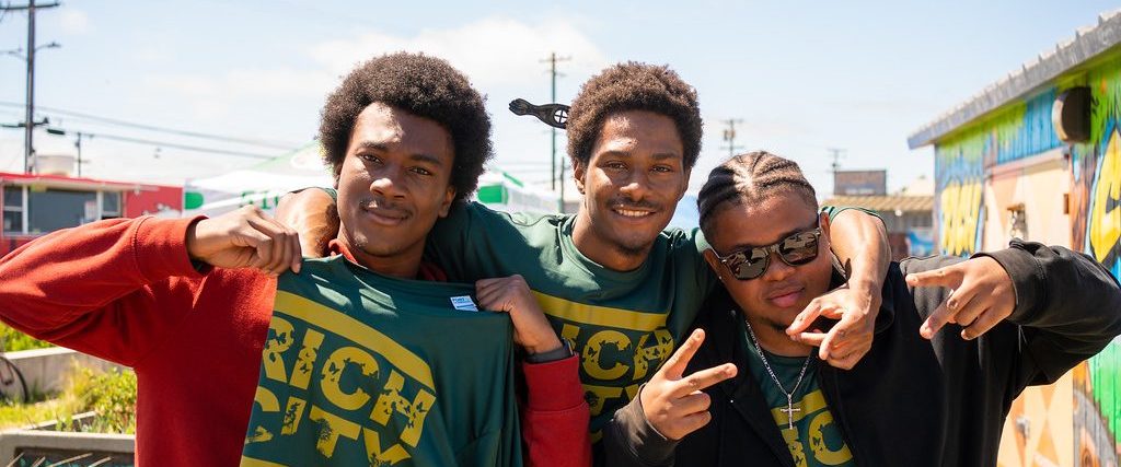Three young guys posing together in t-shirts that say Rich City